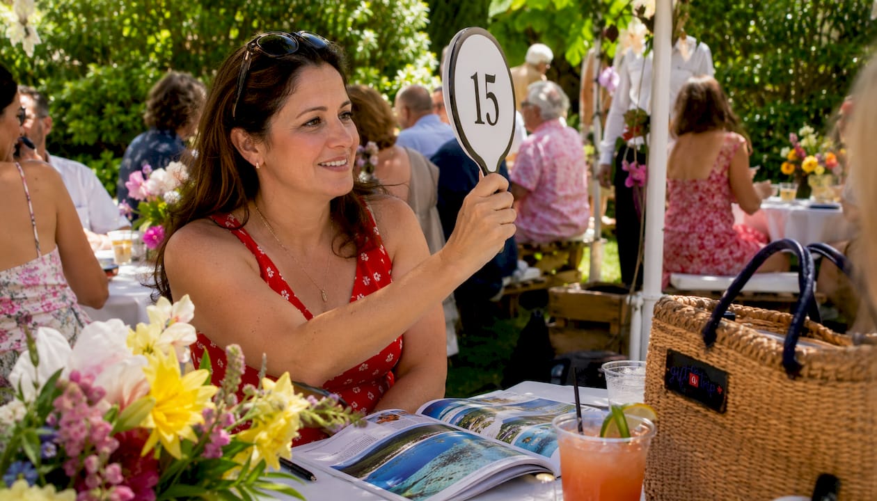 charity event planning tips for travel auctions in 2026 3 woman bidding at outdoor travel charity auction
