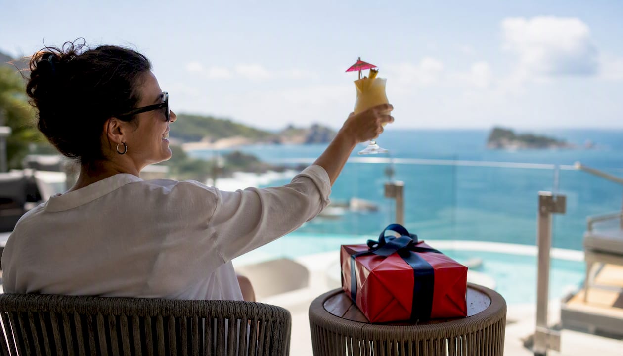 corporate holiday travel gifts: the 2026 hr buyer's guide 4 person holding cocktail on resort balcony with gift box nearby