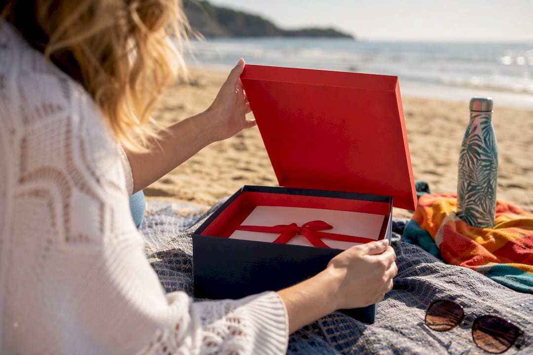 hands opening travel gift box on beach towel